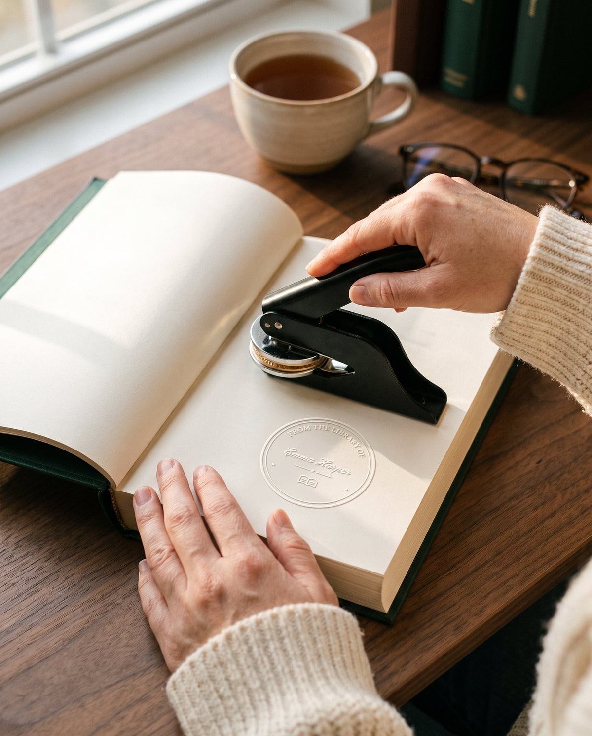 Hands pressing a black personalized book embosser onto the title page of a hardcover book